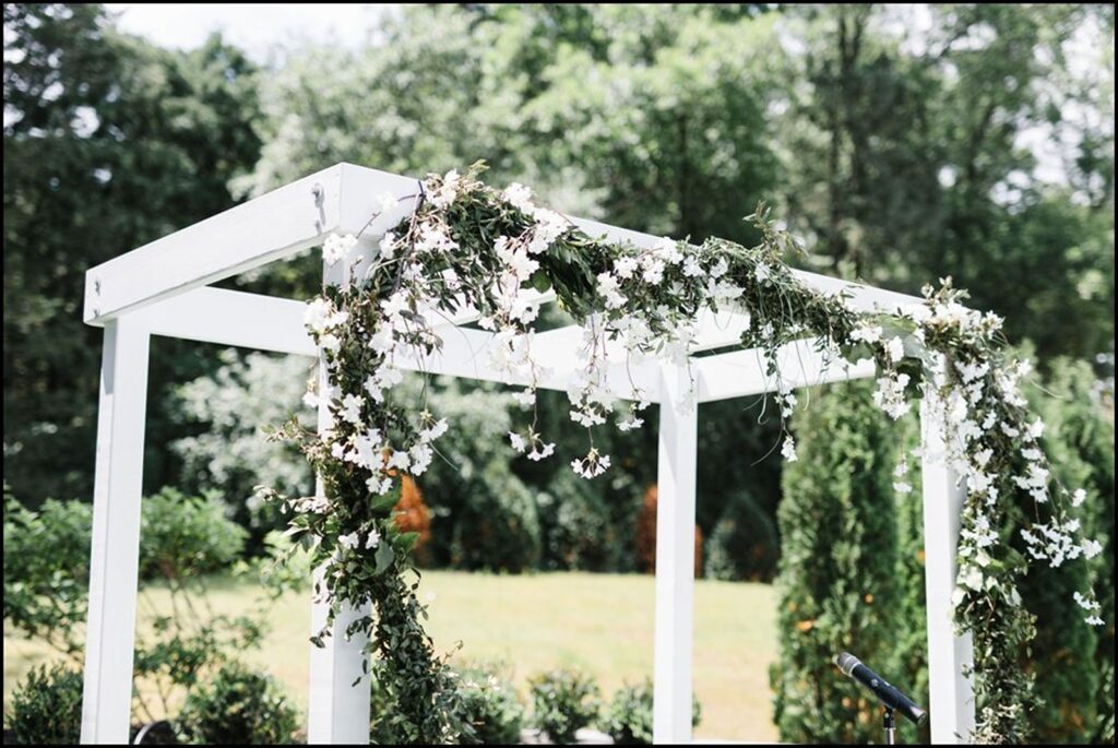 White arbor with floral surrounded by woods for a cocktail reception in the courtyard.